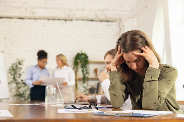 Stressato. Colleghi che lavorano insieme in un ufficio moderno utilizzando dispositivi e gadget durante riunioni creative.