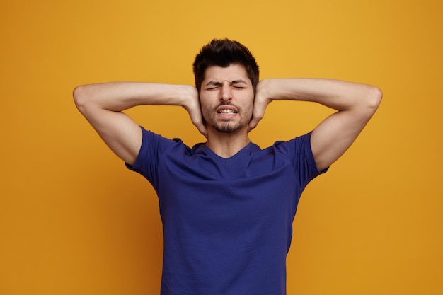 Stressato giovane bell'uomo che chiude le orecchie con le mani con gli occhi chiusi su sfondo giallo