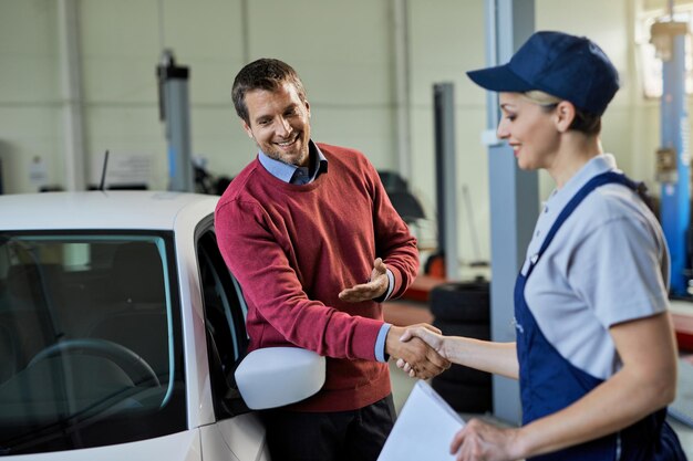 Stretta di mano del cliente soddisfatto con il meccanico femminile nell'officina di riparazioni auto