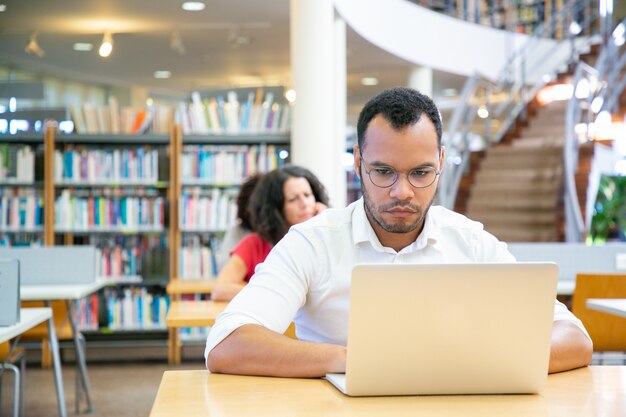 Studente adulto maschio messo a fuoco che effettua ricerca in biblioteca