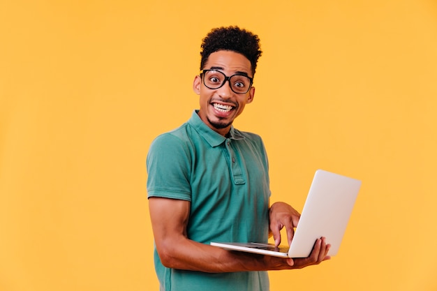 Studente africano ispirato in vetri che tengono computer portatile bianco. sorridente libero professionista maschio nero spensierato.