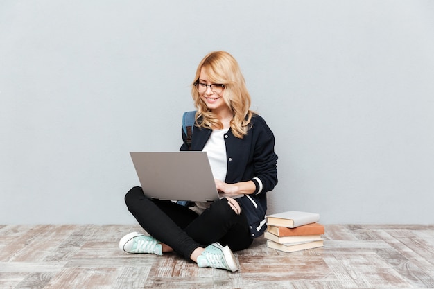 Studente allegro della giovane donna che per mezzo del computer portatile.