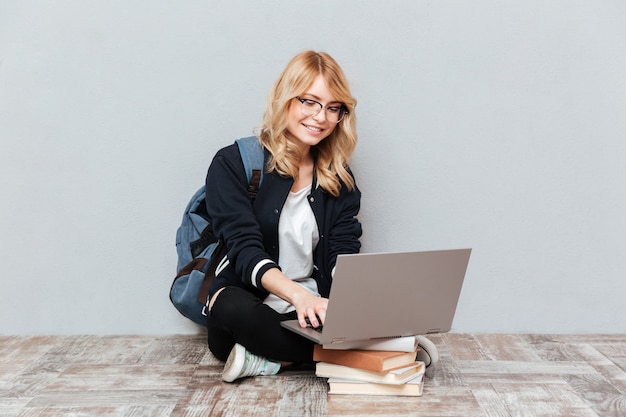 Studente allegro della giovane donna che per mezzo del computer portatile.