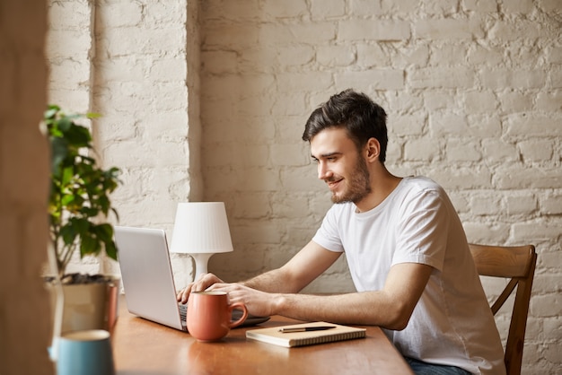 Studente attraente utilizza la tecnologia Internet e la connessione wi-fi ad alta velocità per chattare con un amico