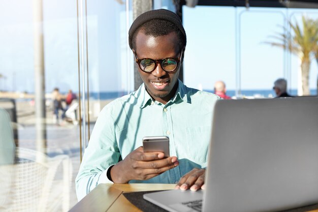 Studente bello che indossa accessori alla moda digitando il messaggio sul telefono cellulare