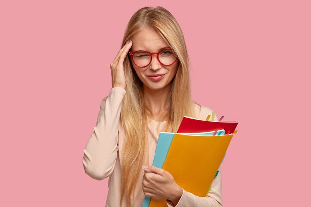 Studente di college biondo smemorato triste che posa contro il muro rosa