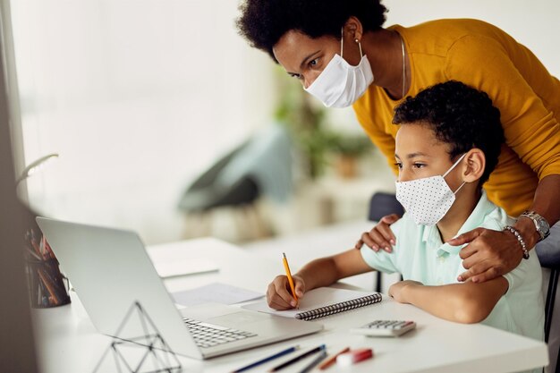 Studente elementare nero che prende appunti mentre elearning da casa durante la pandemia COVID19