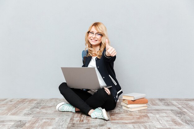 Studente felice della giovane donna che per mezzo del computer portatile.