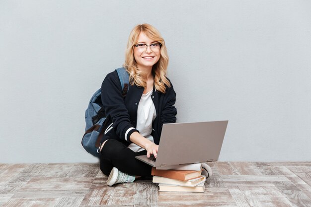 Studente felice della giovane donna che per mezzo del computer portatile.