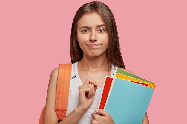 Studente intelligente perplesso in posa contro il muro rosa