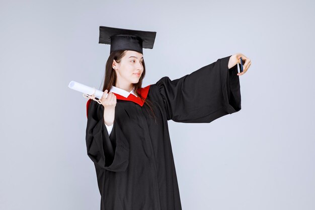Studente laureato grazioso in abito che prende selfie. Foto di alta qualità
