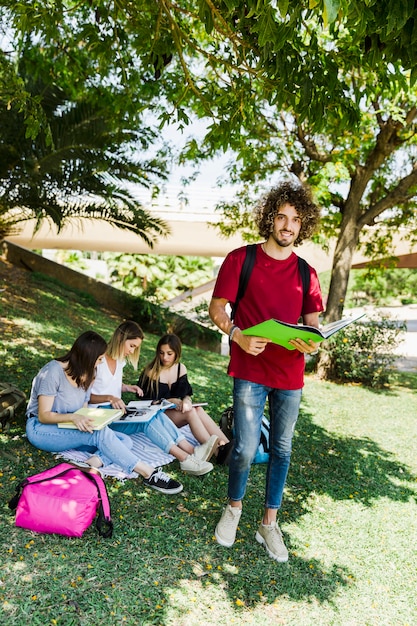 Studente maschio con libro in piedi vicino agli amici