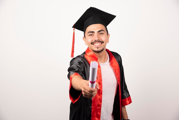 Studente maschio felice che mostra il suo diploma su bianco.