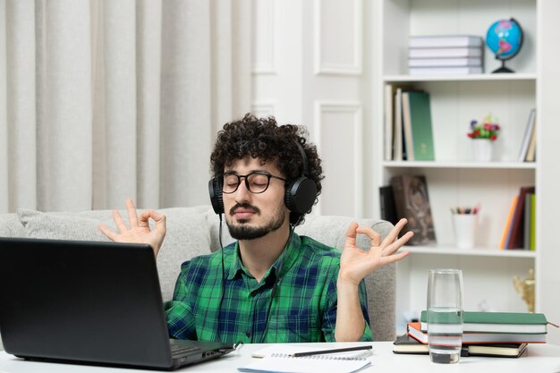 Studente online carino giovane ragazzo che studia al computer con gli occhiali in camicia verde che mostra il segno zen