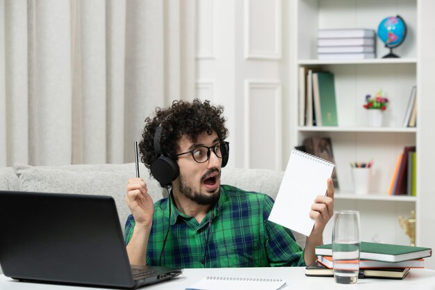 Studente online carino giovane ragazzo che studia al computer con gli occhiali in camicia verde scioccato e sorpreso