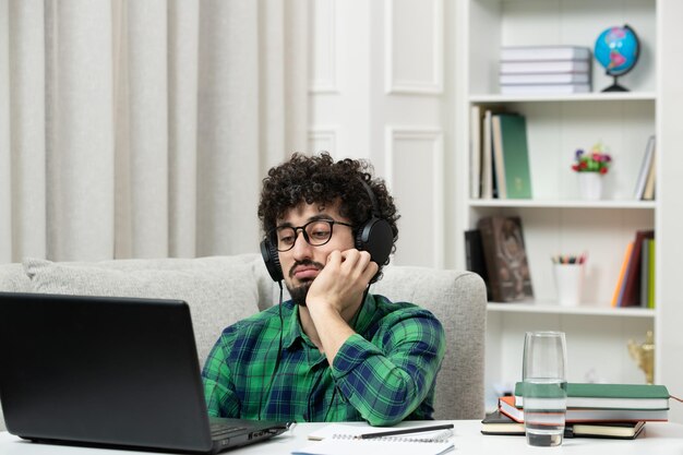 Studente online carino giovane ragazzo che studia sul computer con gli occhiali in camicia verde ascolto stanco