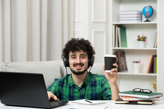 Studente online carino giovane ragazzo che studia sul computer con gli occhiali in camicia verde che tiene una tazza