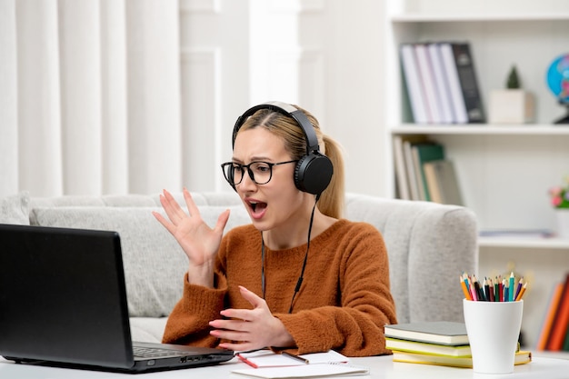 Studente online giovane ragazza carina con gli occhiali e maglione arancione che studia sul computer urlando