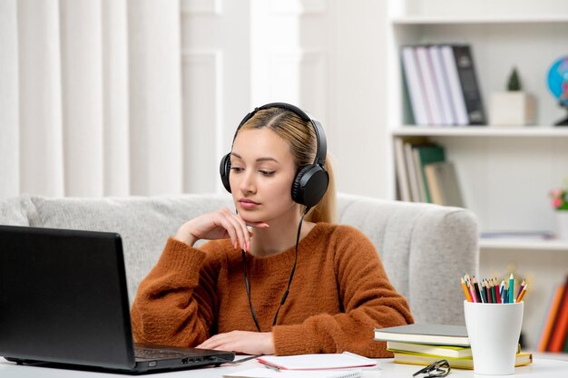 Studente online ragazza carina con gli occhiali e maglione che studia sul computer pensando e ascoltando