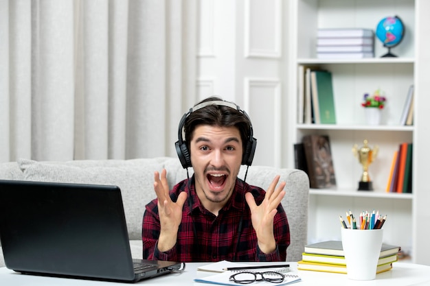 Studente online ragazzo carino in camicia a quadri con gli occhiali che studia al computer eccitato per i voti