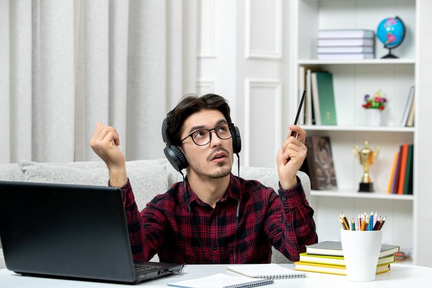 Studente online ragazzo carino in camicia a quadri con gli occhiali che studia sul computer guardando in alto