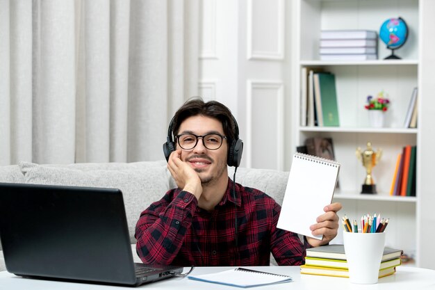 Studente online ragazzo carino in camicia a quadri con gli occhiali che studia sul computer sorridente e sicuro di sé