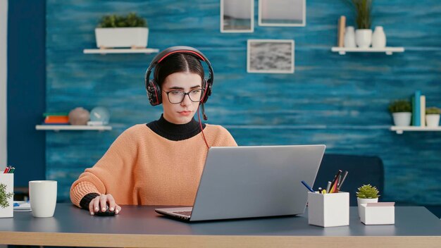 Studente universitario che utilizza cuffie e laptop per partecipare a una lezione online durante una riunione di videochiamata. Donna che parla con l'insegnante in videoconferenza remota per la comunicazione educativa dal vivo.