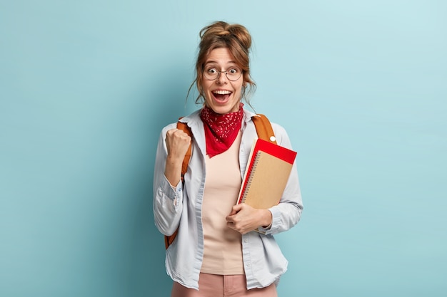 Studente universitario con espressione felice, alza il pugno chiuso, festeggia l'esame superato con successo, riceve un voto eccellente