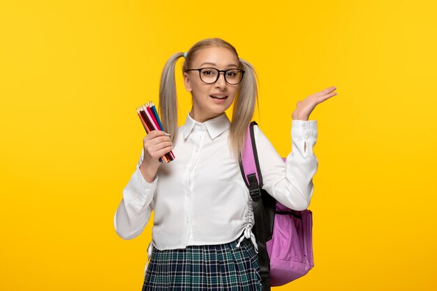 Studentessa bionda tifo per la giornata mondiale del libro con code di cavallo su sfondo giallo che tiene molte matite