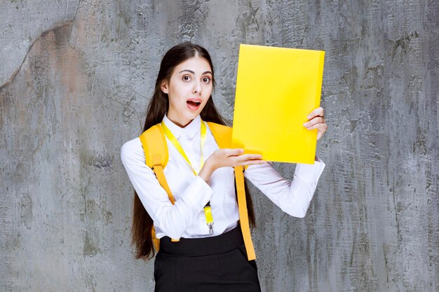 Studentessa che indossa il blocco note della tenuta dello zaino giallo. Foto di alta qualità