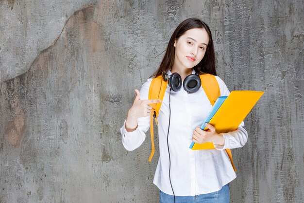 Studentessa con zaino e cuffie che puntano al libro. Foto di alta qualità