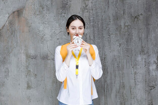 Studentessa di college femminile con lo zaino giallo che tiene l'orologio. Foto di alta qualità