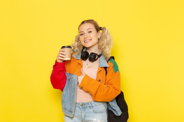 studentessa giovane in abiti moderni tenendo il caffè e sorridente sul giallo