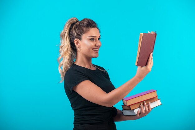 Studentessa in possesso di un pesante stock di libri e leggendone uno.