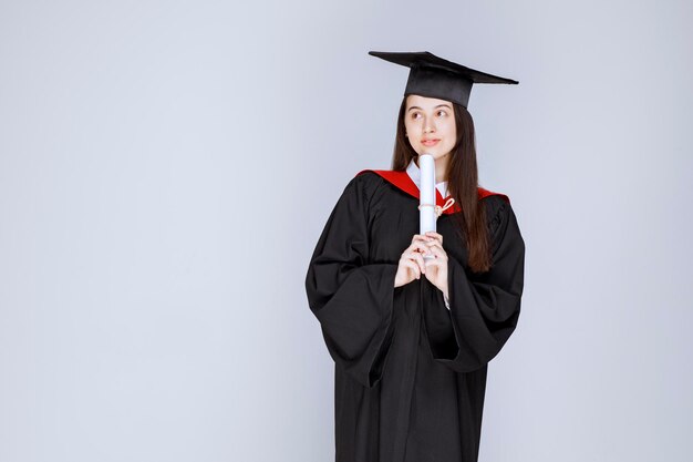 Studentessa laureata in abito con in piedi certificato universitario. Foto di alta qualità