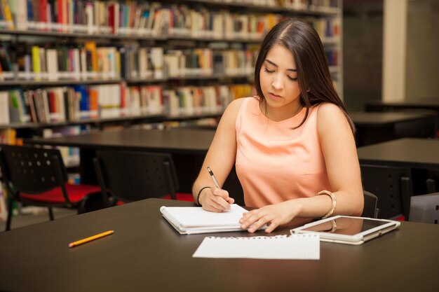 Studentessa universitaria graziosa che fa un po' di lavoro alla biblioteca della scuola