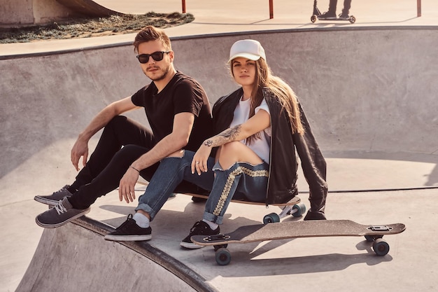 Studenti alla moda e alla moda sono seduti al soleggiato skatepark con i loro longboard. Ci sono altri skatebordisti in background.