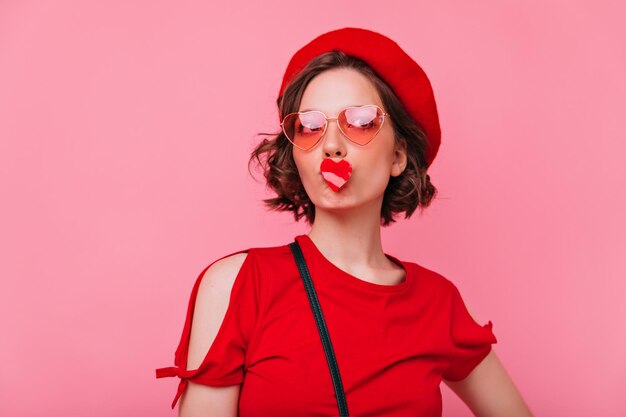 Studio di una donna caucasica agghiacciante in un berretto alla moda Giovane donna bianca attraente che scherza su sfondo pastello