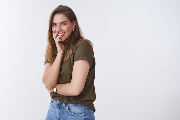 Studio shot carismatico entusiasta ridacchiando giovane ragazza che si diverte a deridere scherzare ridendo ad alta voce profilo in piedi girando la fotocamera sorridente divertito, coprendo la bocca sfondo bianco