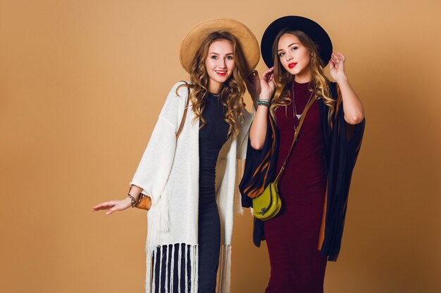 Studio shot di caduta di due modelli con acconciatura ondulata bionda in lana e cappello di paglia che indossa un poncho a righe