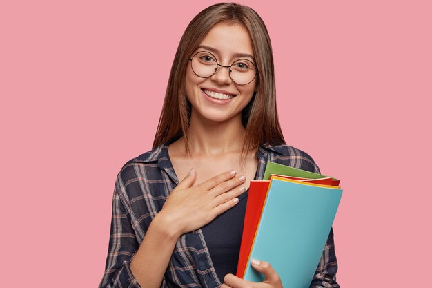 Studio shot di carino grato giovane imprenditrice in posa contro il muro rosa con gli occhiali