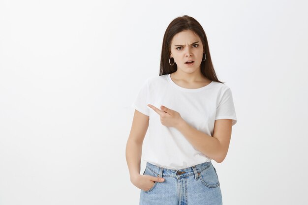 Studio shot di dubbiosa giovane donna in posa contro il muro bianco