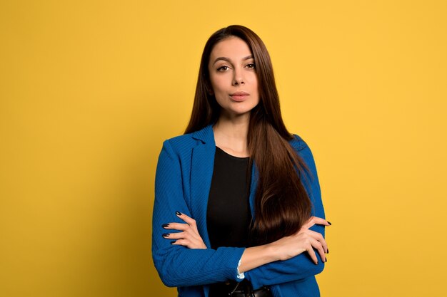 Studio shot di giovane donna sicura di sé con lunghi capelli scuri che indossa giacca blu in posa