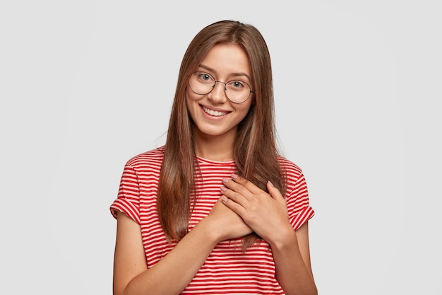 Studio shot di tenera donna amichevole esprime dolci ringraziamenti, si scioglie con parole piacevoli, tiene le mani sul plam