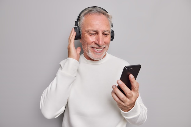 Studio shot di un bell'uomo anziano che usa gadget moderni e ascolta la musica preferita tramite le cuffie