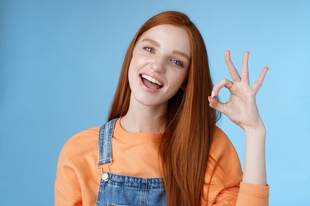 Studio shot spensierato felice attraente ragazza rossa europea mostra ok segno ok sorridente denti bianchi approvazione conferma consiglio buon prodotto accordo termini dare feedback positivo, pensare idea perfetta.