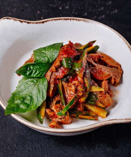 Stufato di carne di verdure con foglie di basilico in una ciotola bianca.