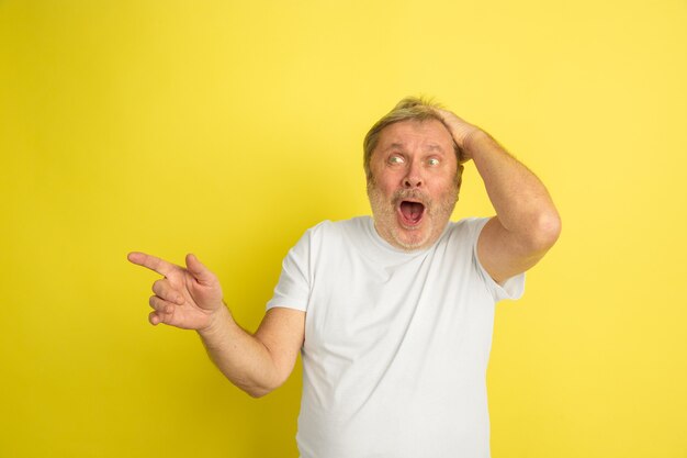 Stupito, scioccato, indicando di lato. Ritratto di uomo caucasico isolato su sfondo giallo studio. Bello modello maschio in posa della camicia bianca. Concetto di emozioni umane, espressione facciale, vendite, annuncio.