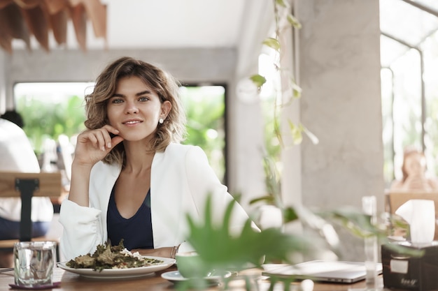 Stylush successo ambizioso attraente giovane femmina specialista di marketing sedersi ristorante moderno caffè mangiare insalata sana bere caffè sorridente felice incontro di lavoro durante il pranzo, discutere di lavoro.