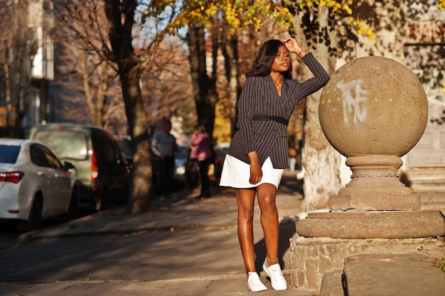 Successo elegante donna afroamericana in giacca e gonna poste in una soleggiata giornata autunnale in strada